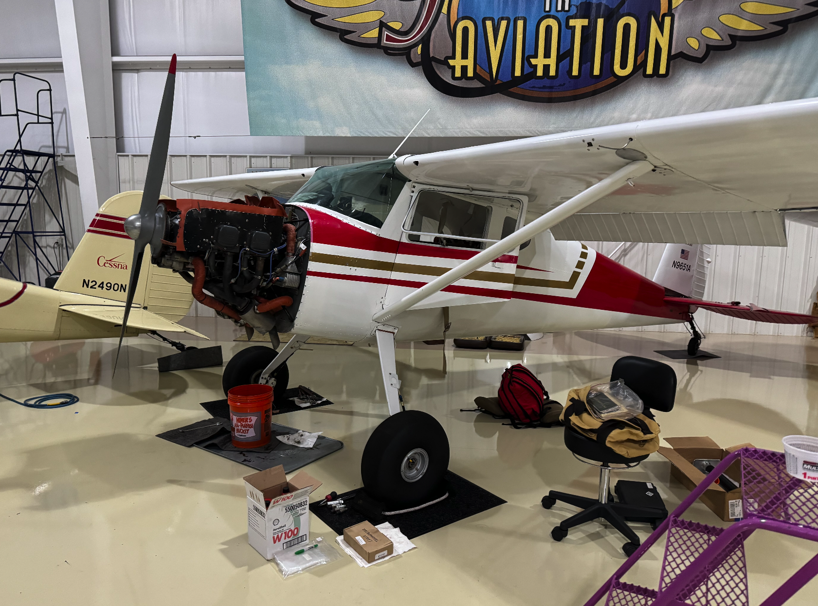 Small aircraft inside a hangar with tools and equipment around it, partially disassembled with the engine exposed.
