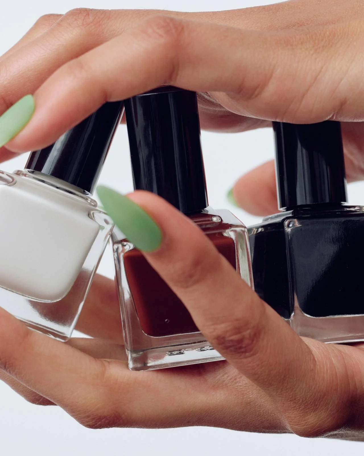 a close up view of two hands with green nails holding 3 different  colors of nail polish