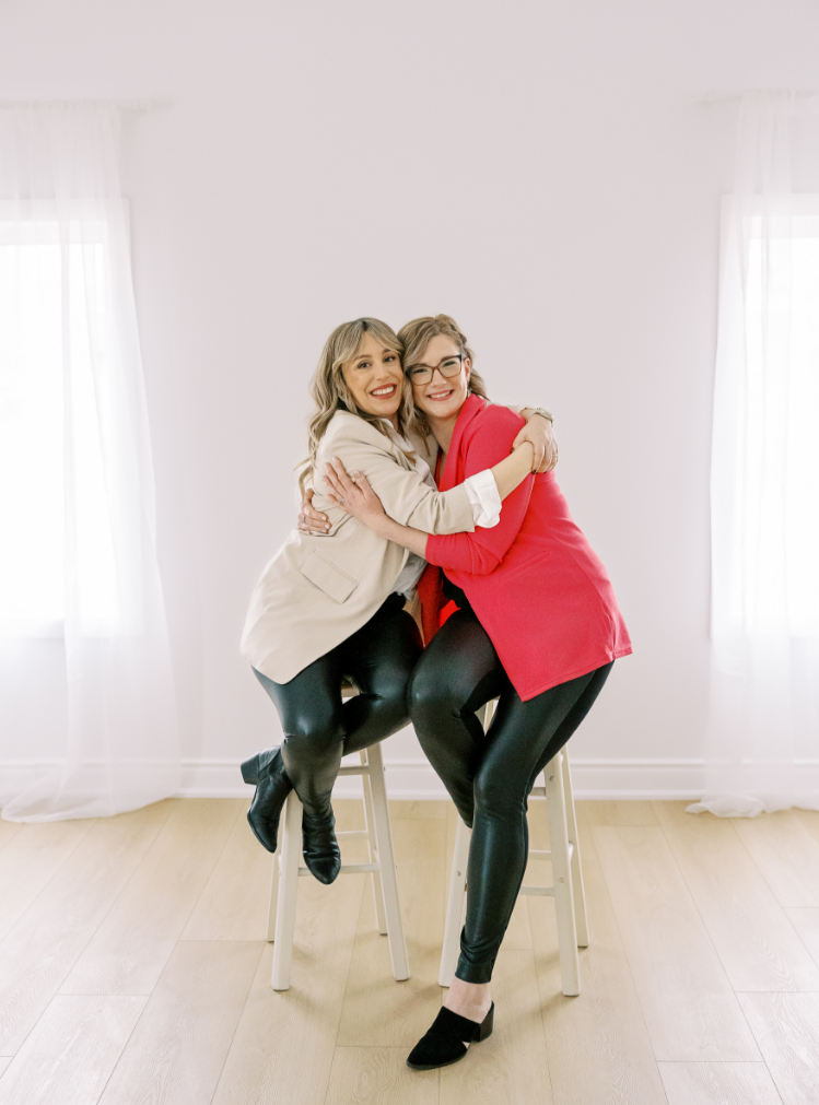 Freebird owners Candice and Lindsey hugging each other while sitting on wooden stools.