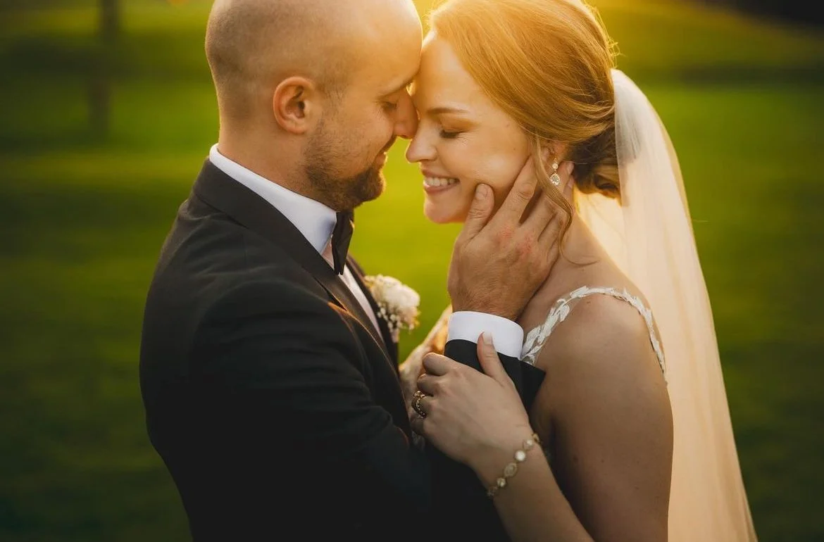 Bride and groom embracing in a park during sunset.