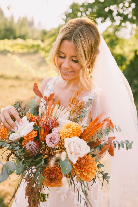 Bride holding a vibrant autumn bouquet with orange, white, and pink flowers, outdoors