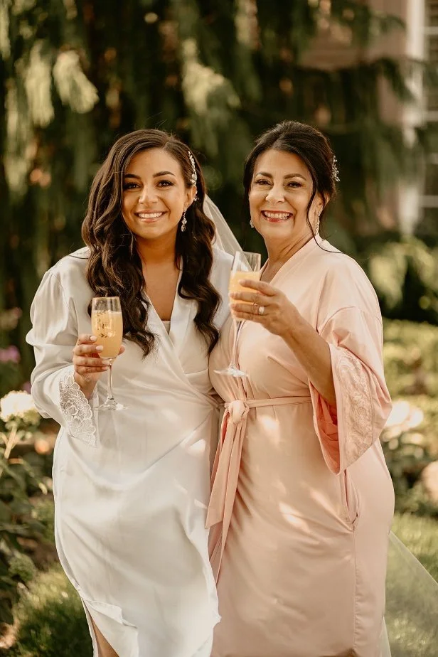 Two women in robes smiling and holding glasses outdoors.