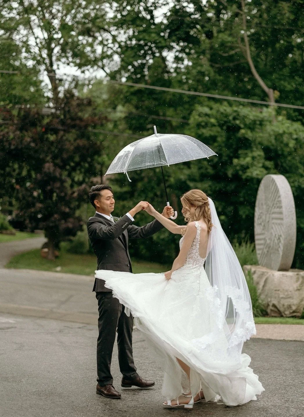 Bride and groom dancing under an umbrella in the rain outdoors.
