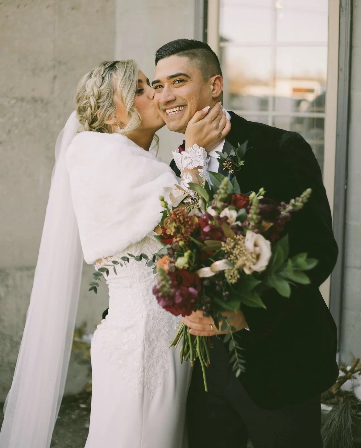 Bride kissing groom on the cheek holding a bouquet