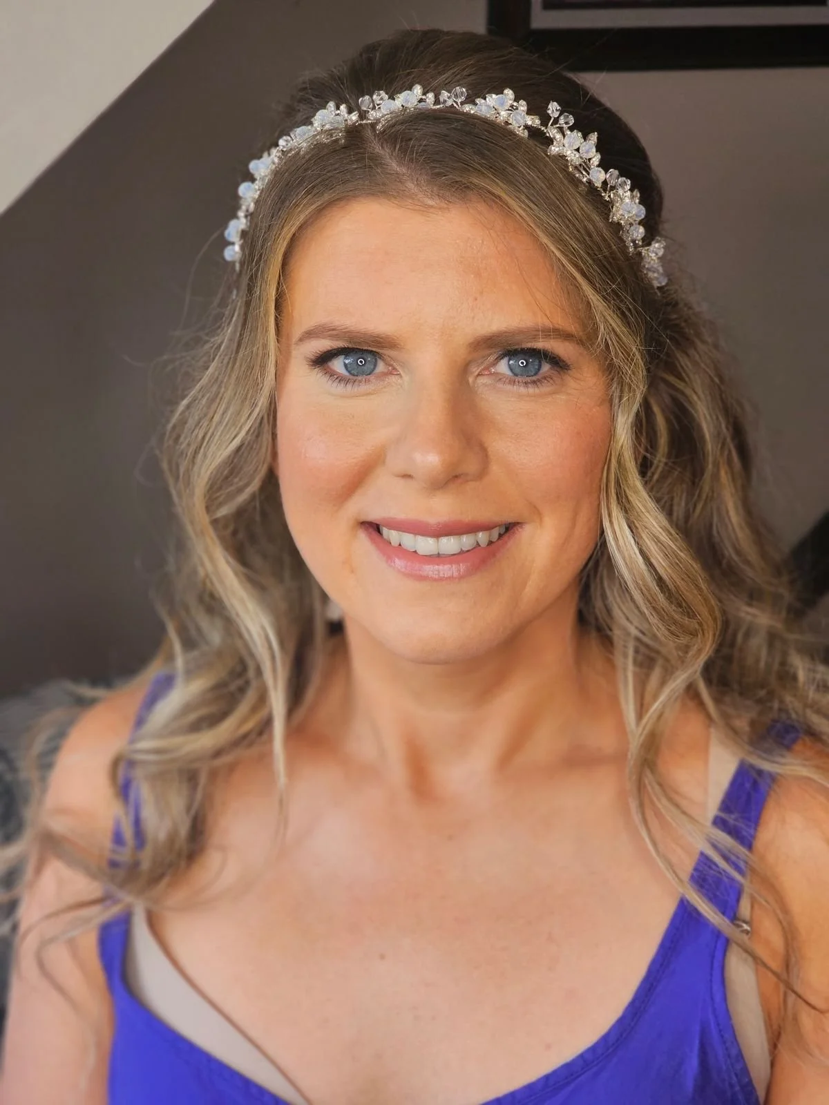 Smiling woman with long wavy hair wearing a crystal headband and a blue top.