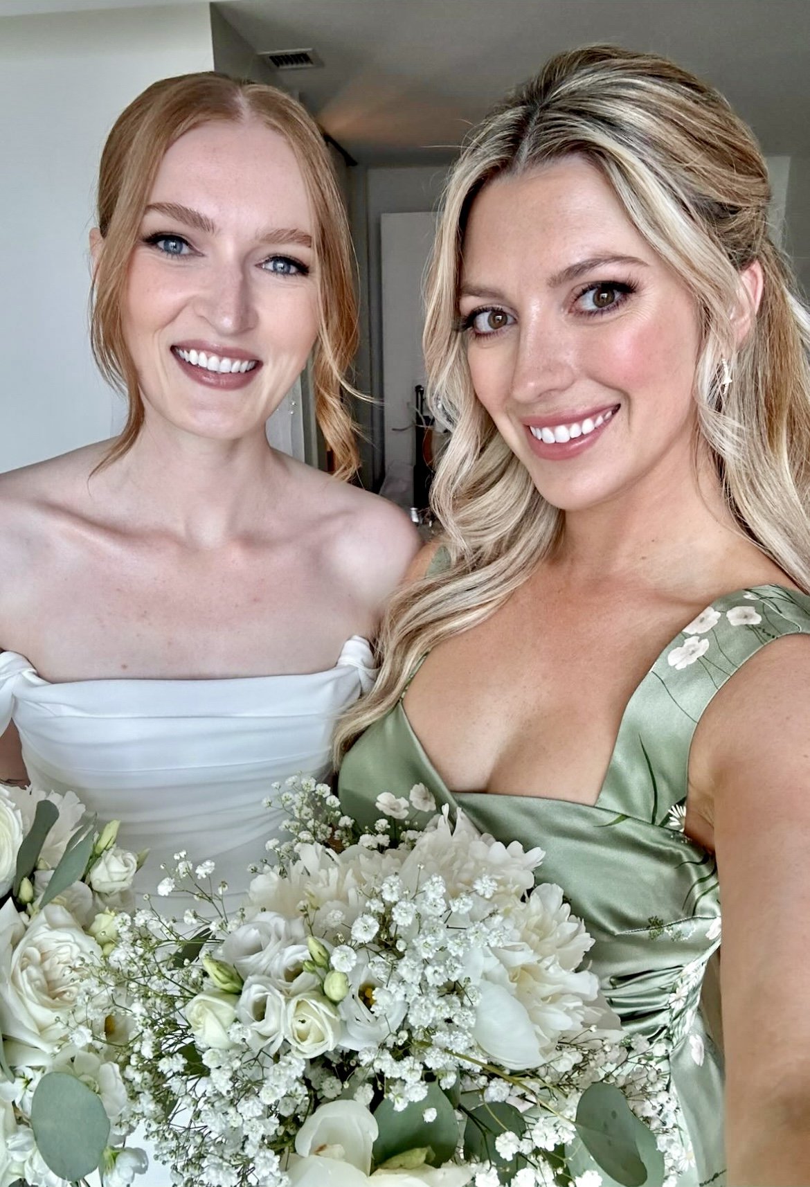 Two women smiling, dressed in formal attire, holding bouquets of white flowers.