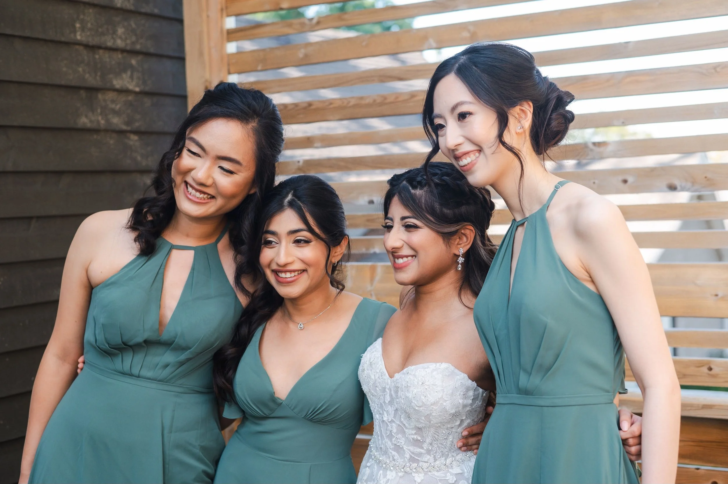 Bride with three bridesmaids in green dresses posing together.