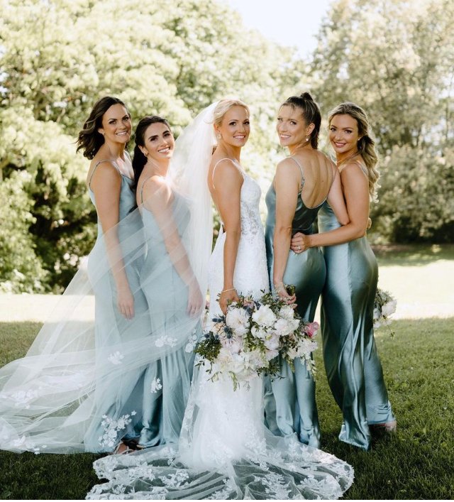 Bridal party with bridesmaids in blue dresses and bride in a white gown holding bouquets, posing outdoors.