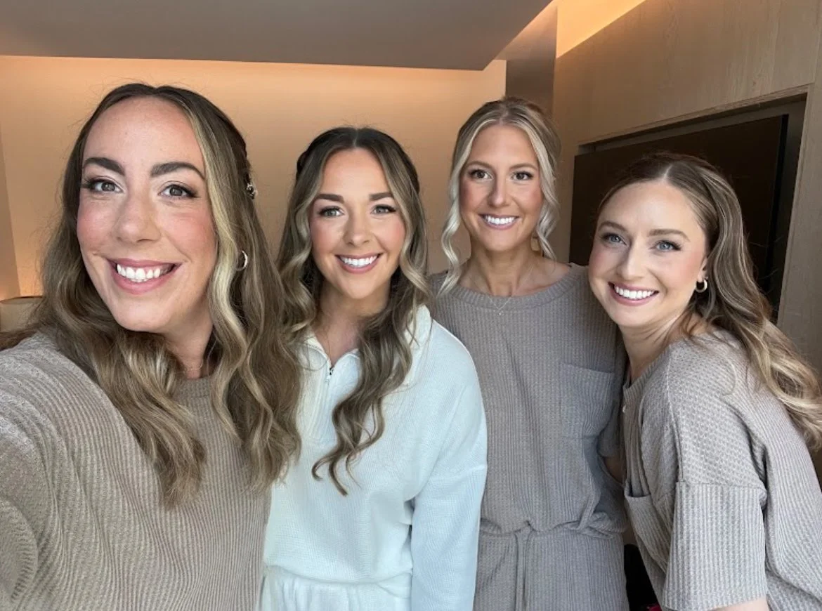 Four women smiling indoors wearing casual outfits.