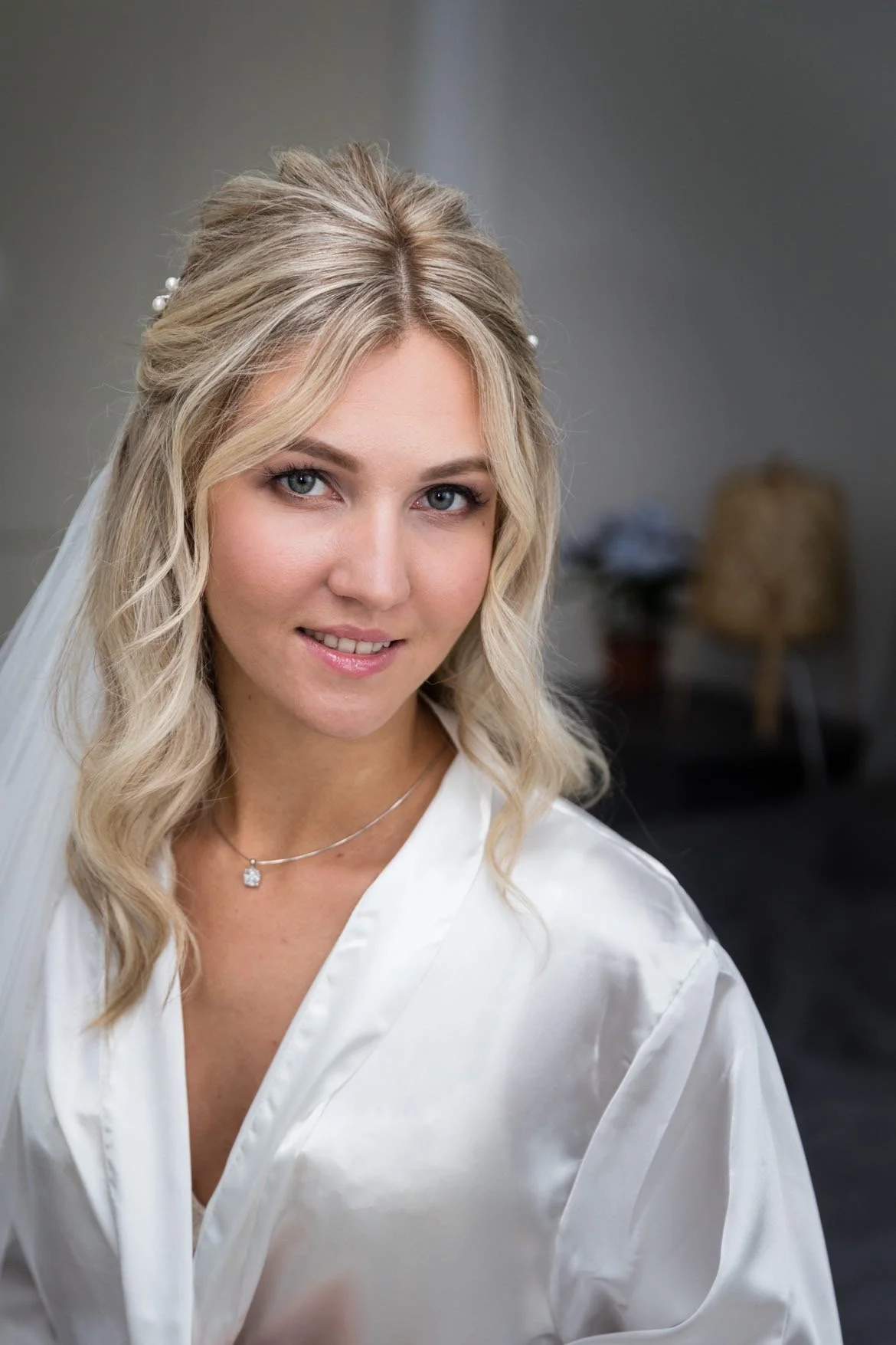 Portrait of a woman with blonde hair, wearing a white robe and a necklace.