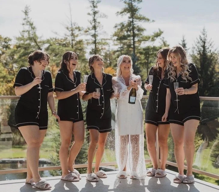 Bride with bridesmaids in matching black pajamas, holding champagne glasses.