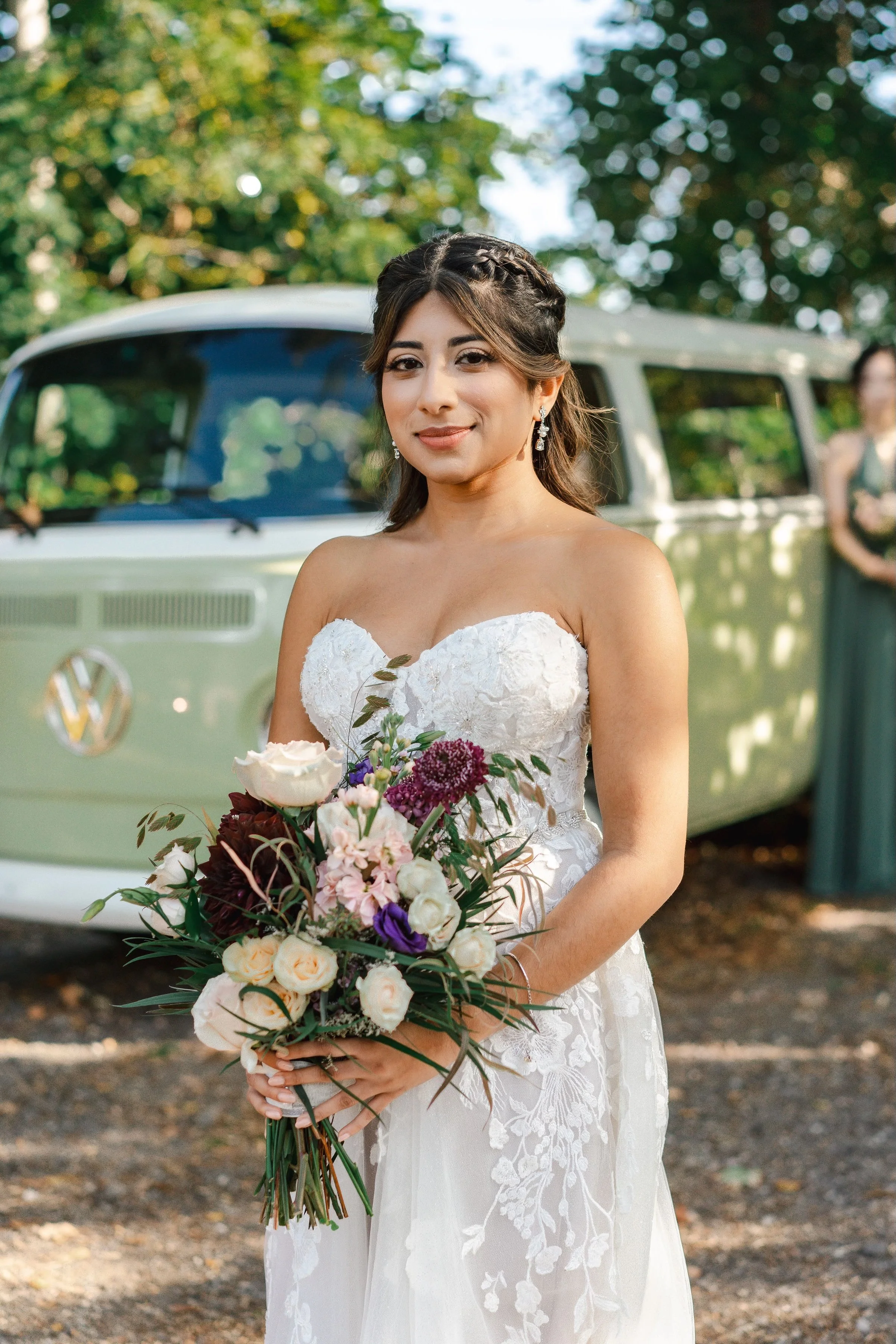 Bride in white lace dress holding a bouquet, standing in front of a vintage Volkswagen van.