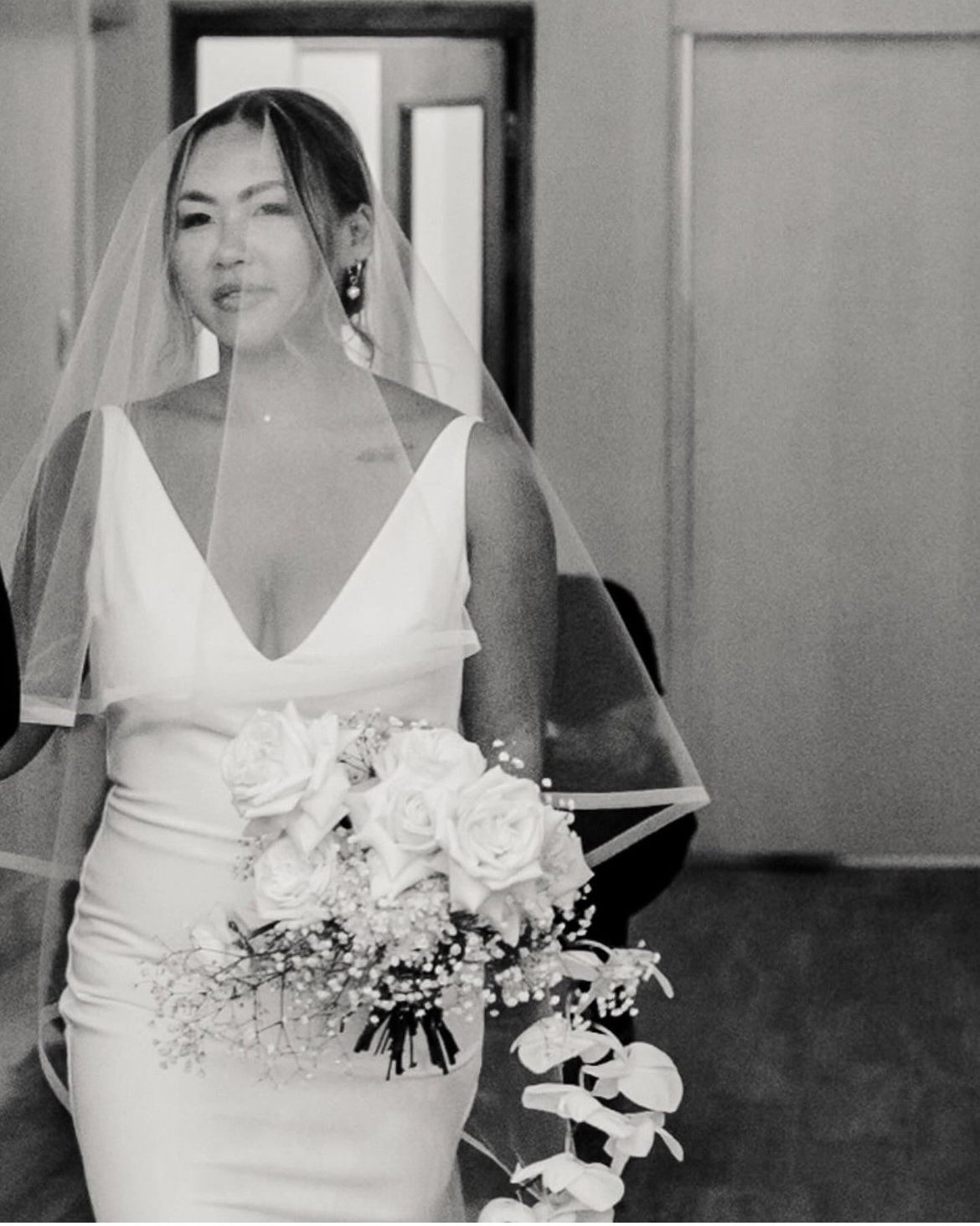 Bride wearing a wedding dress and veil, holding a bouquet of white flowers.
