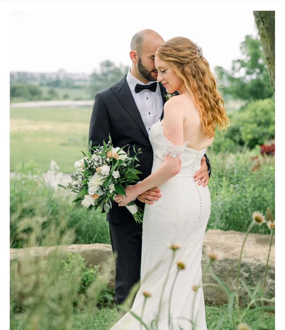 Bride and groom embracing in garden setting, bride holding a bouquet.