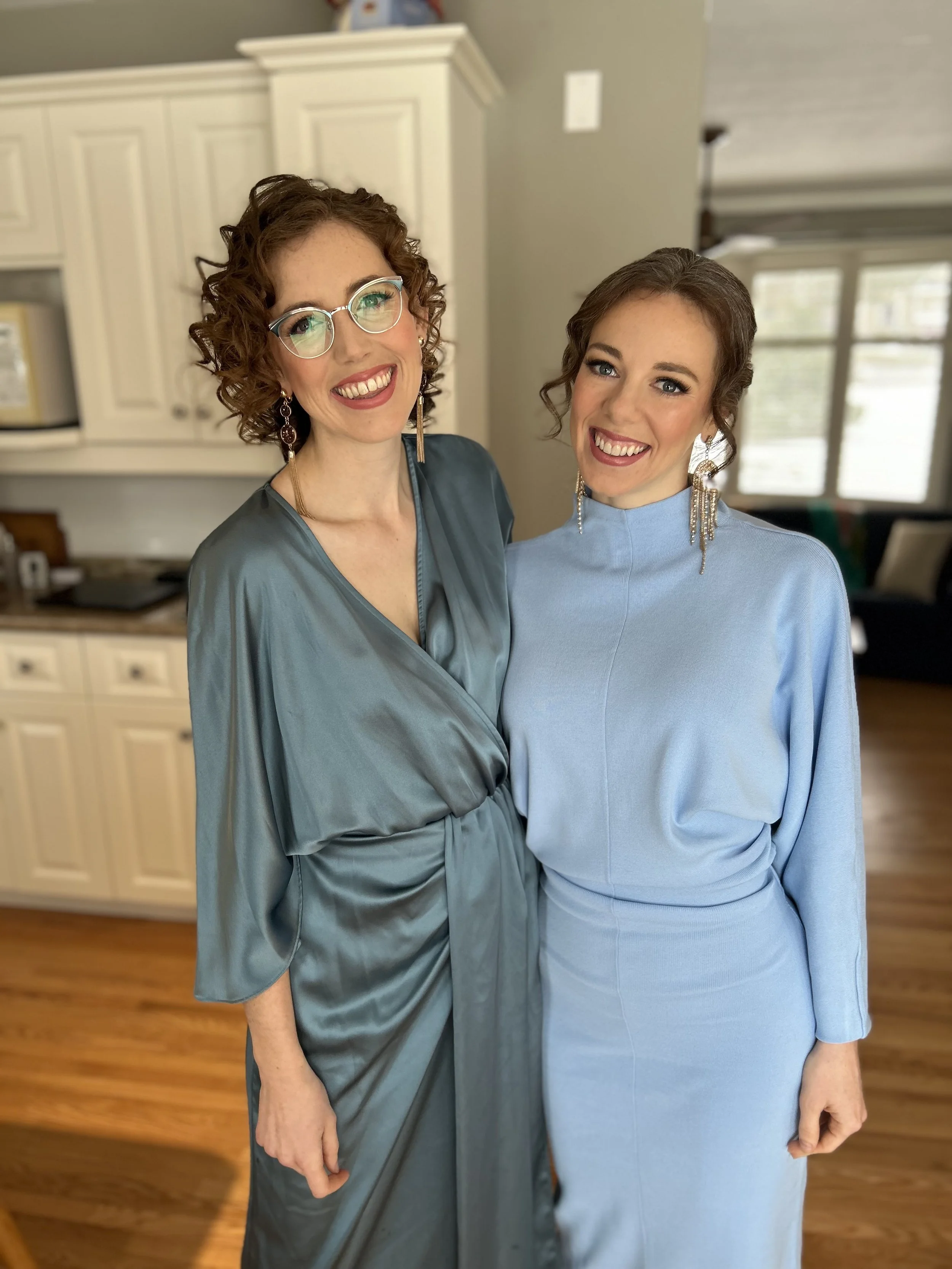 Two women in elegant dresses standing indoors and smiling.