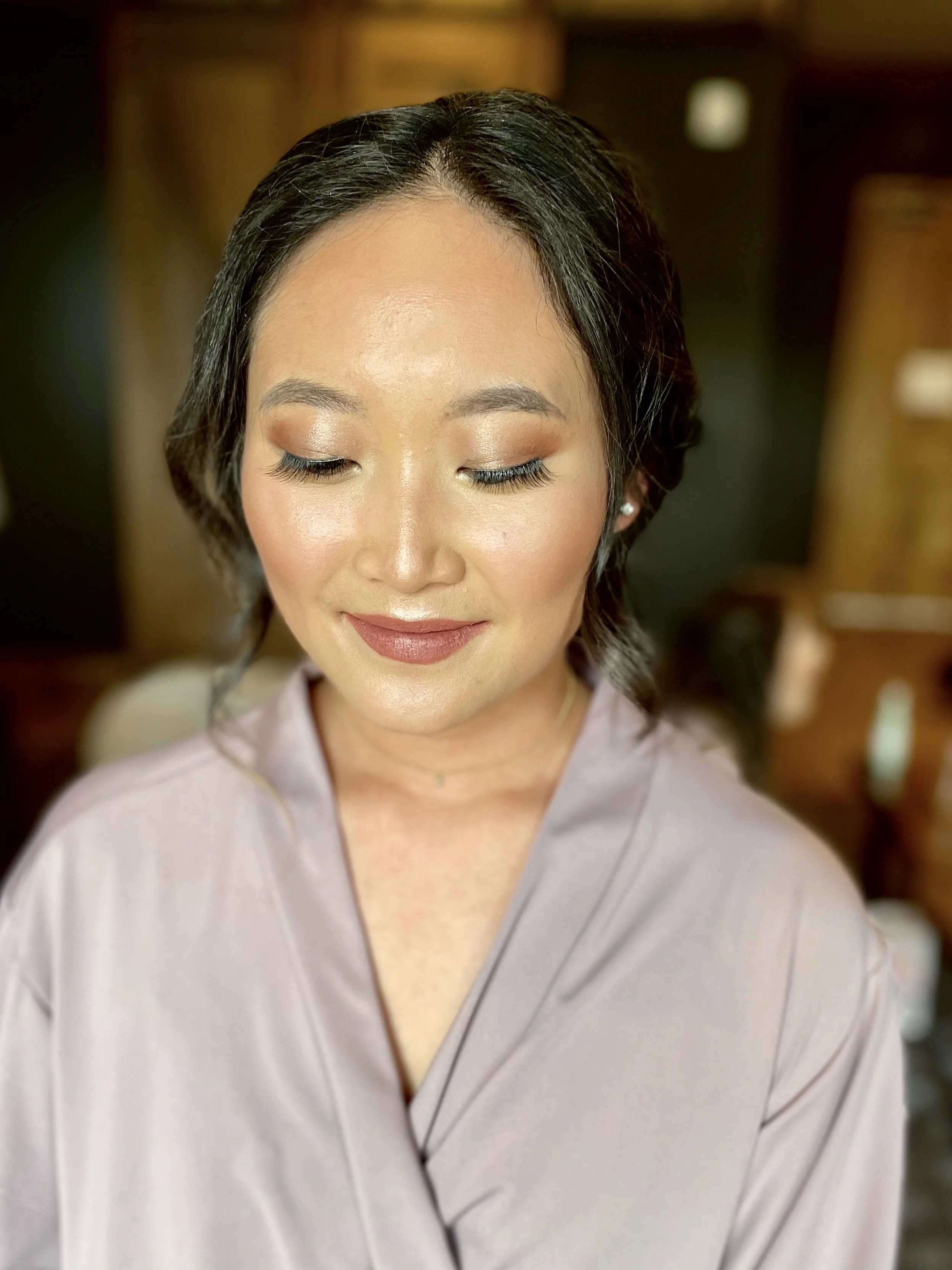 Woman with closed eyes and styled dark hair wearing a light purple robe, showcasing natural makeup.