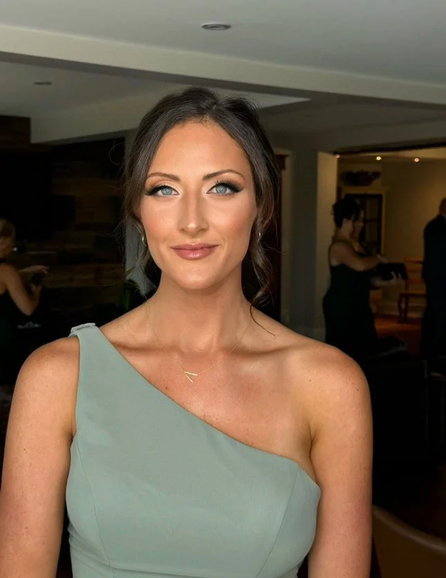Woman in one-shoulder dress smiling indoors.