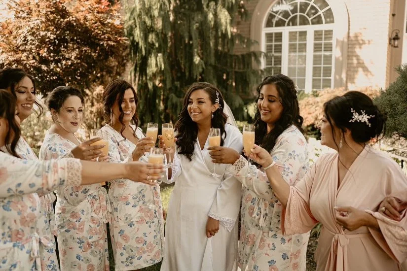 Bridal party in robes toasting with mimosas outdoors.