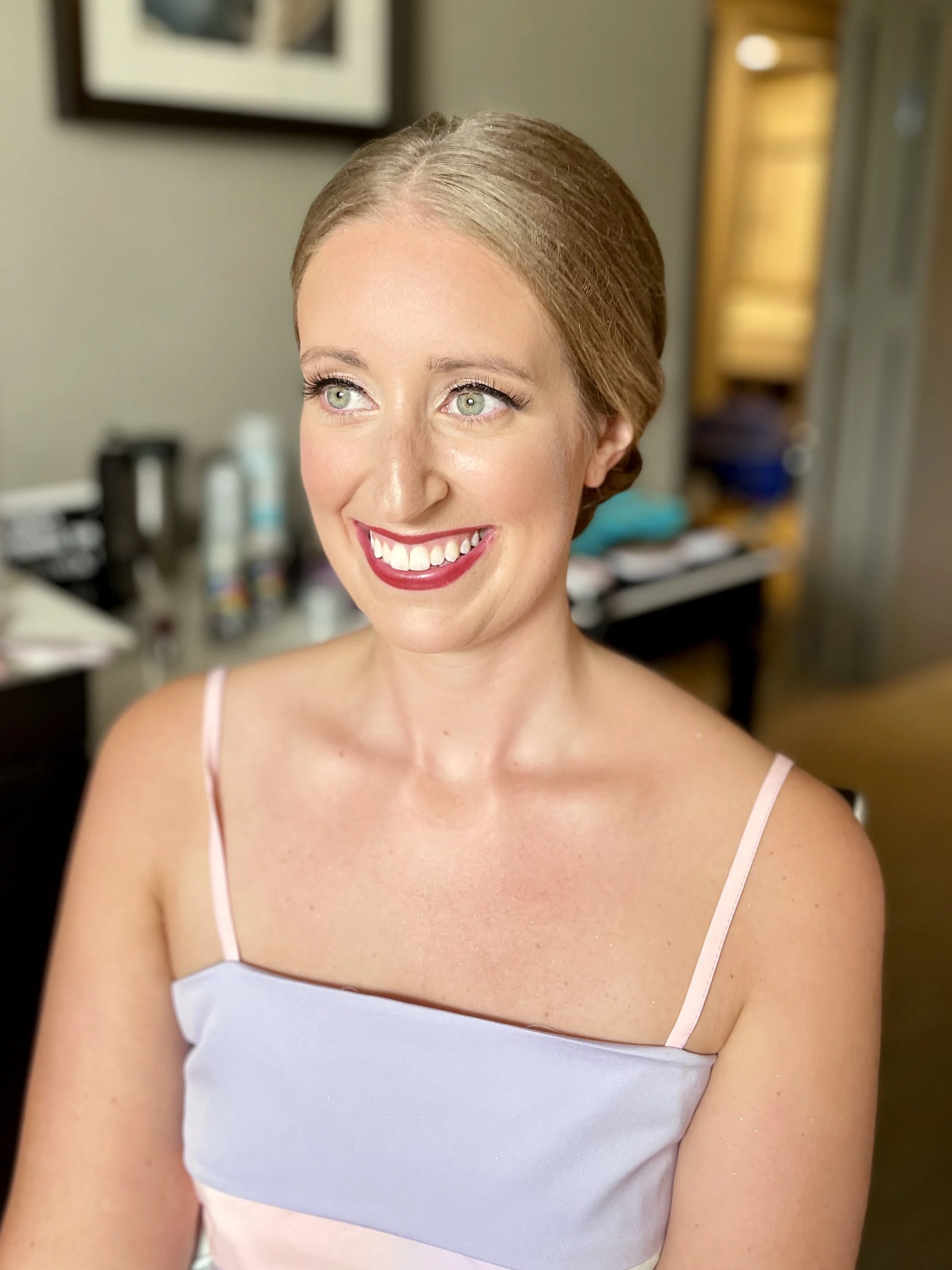 Woman smiling indoors with styled hair and makeup