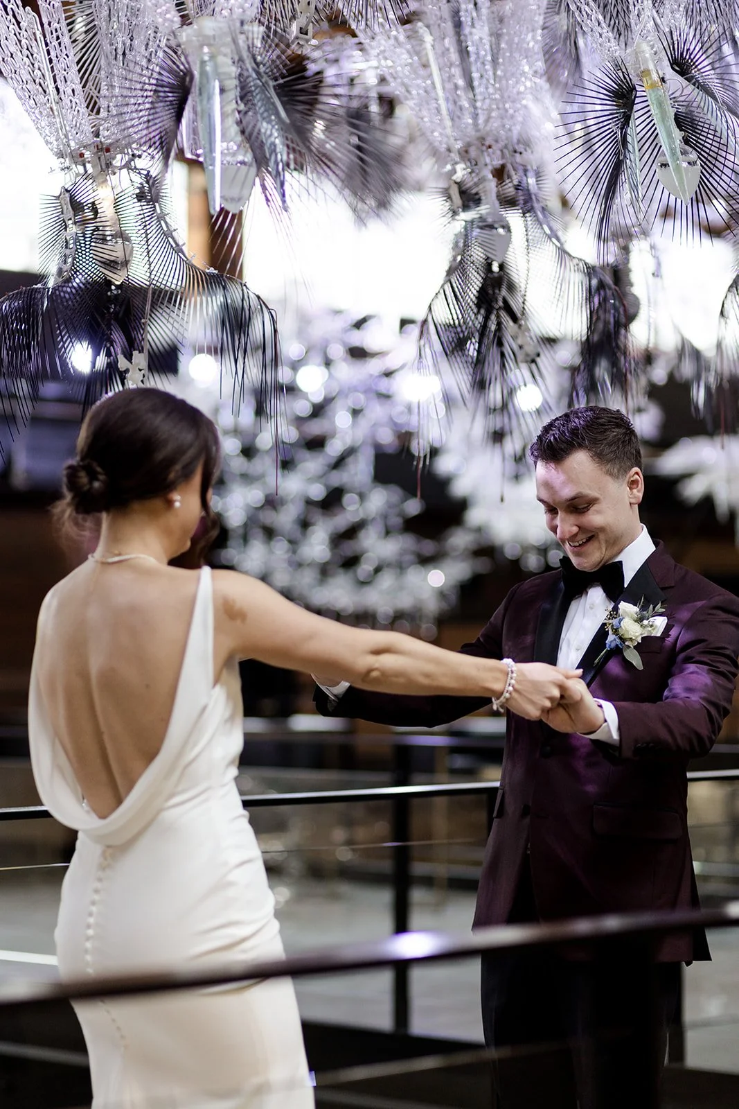 A bride and groom dancing at their wedding reception, with decorative hanging silver and purple ornaments overhead.