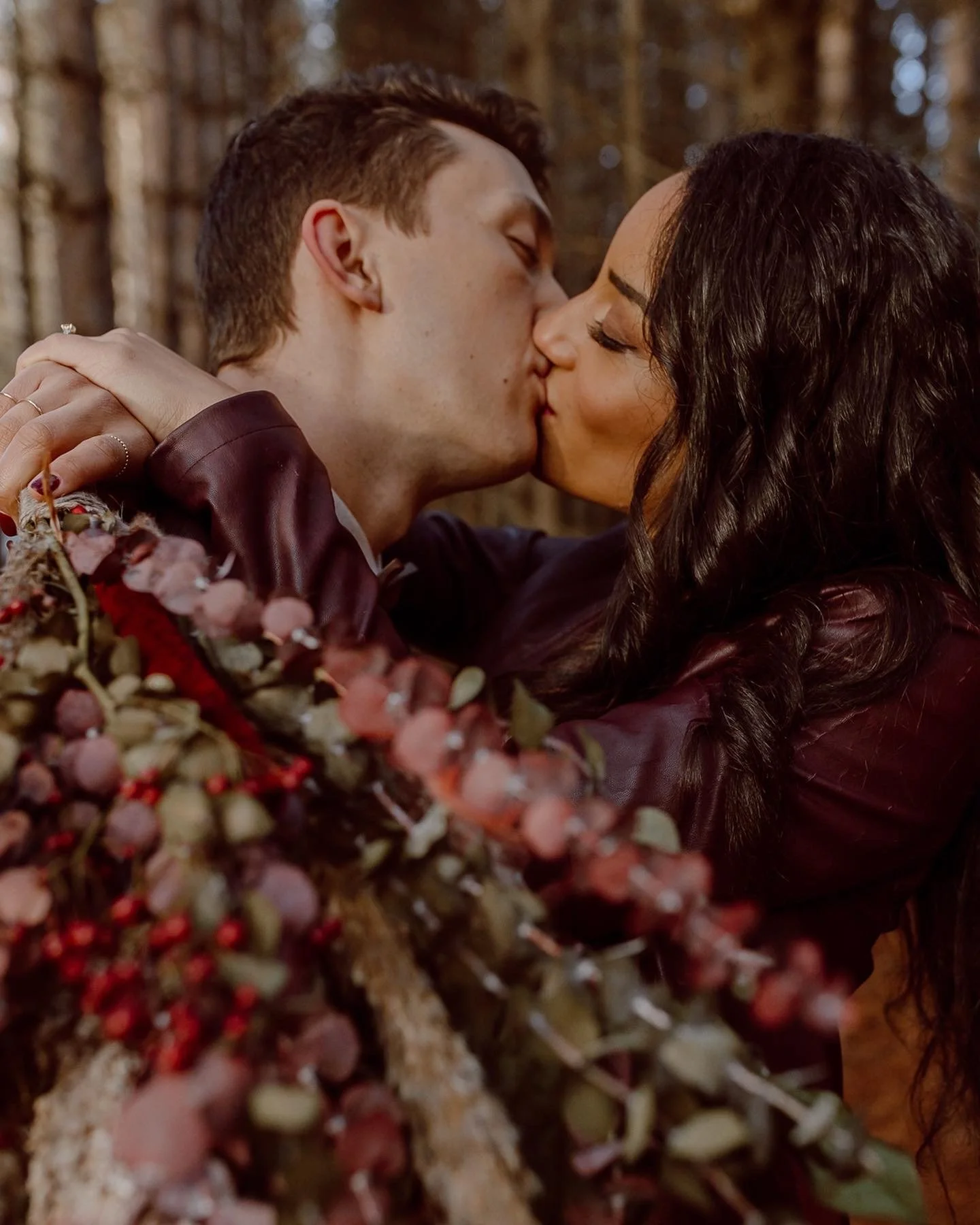 Couple kissing in a forest, surrounded by colorful flowers and wearing leather jackets.