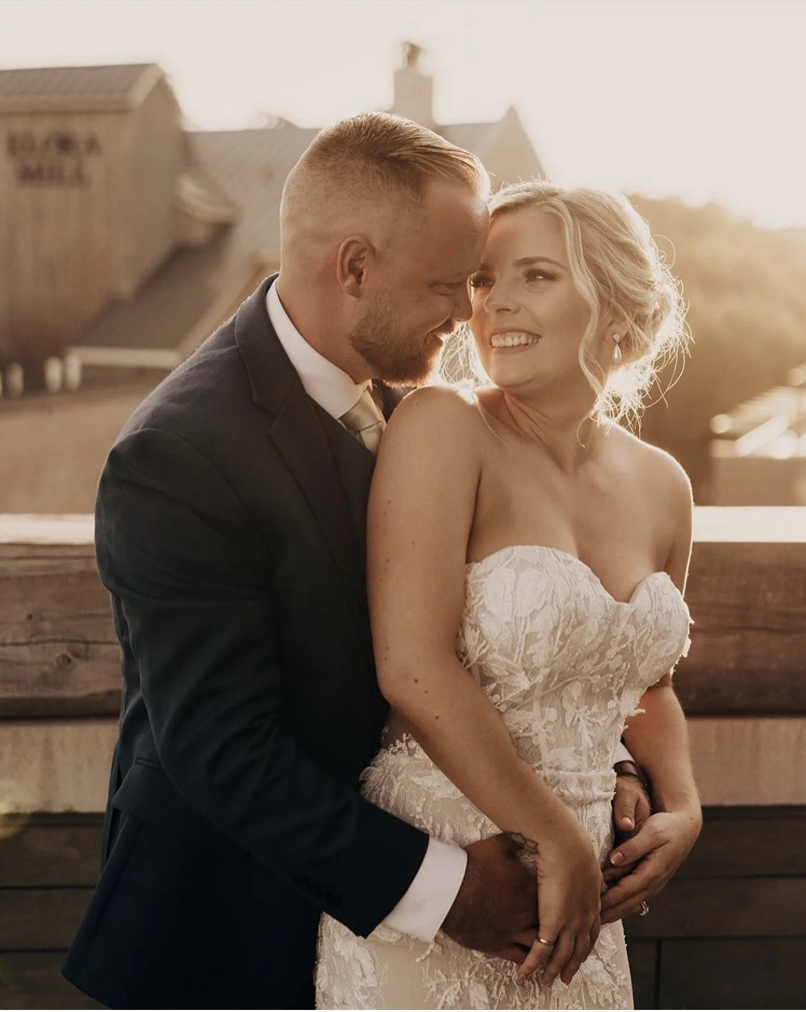 Bride and groom embracing at sunset, smiling.