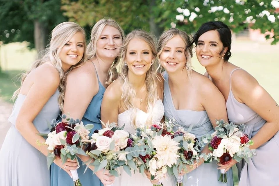 Group of bridesmaids in pastel dresses holding bouquets outdoors.