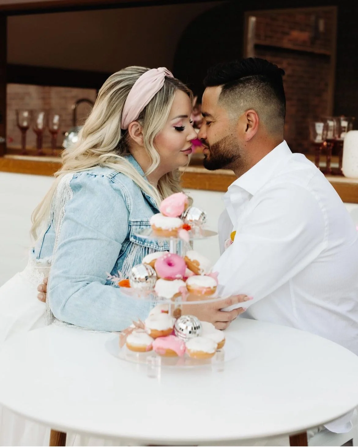 A couple sitting at a table with a tiered stand of pink and white frosted donuts.