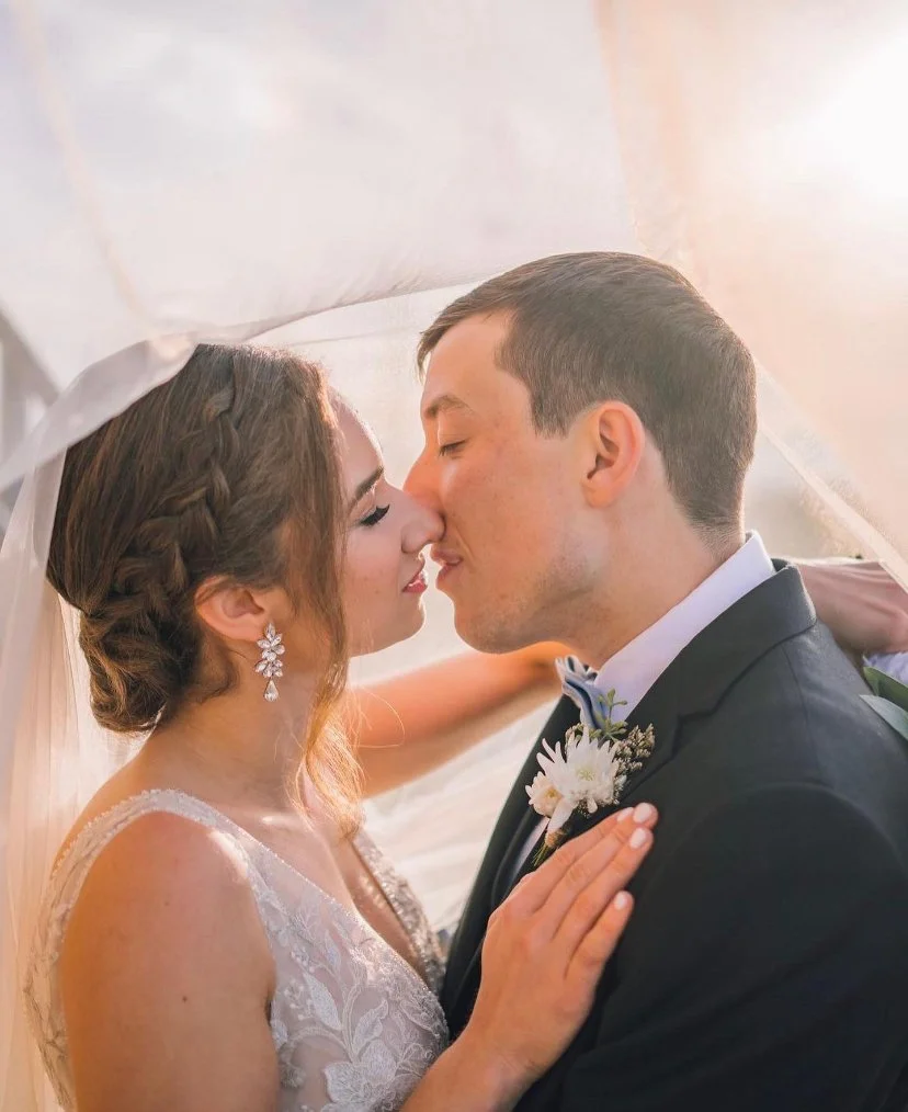Bride and groom kissing under a veil during a wedding.