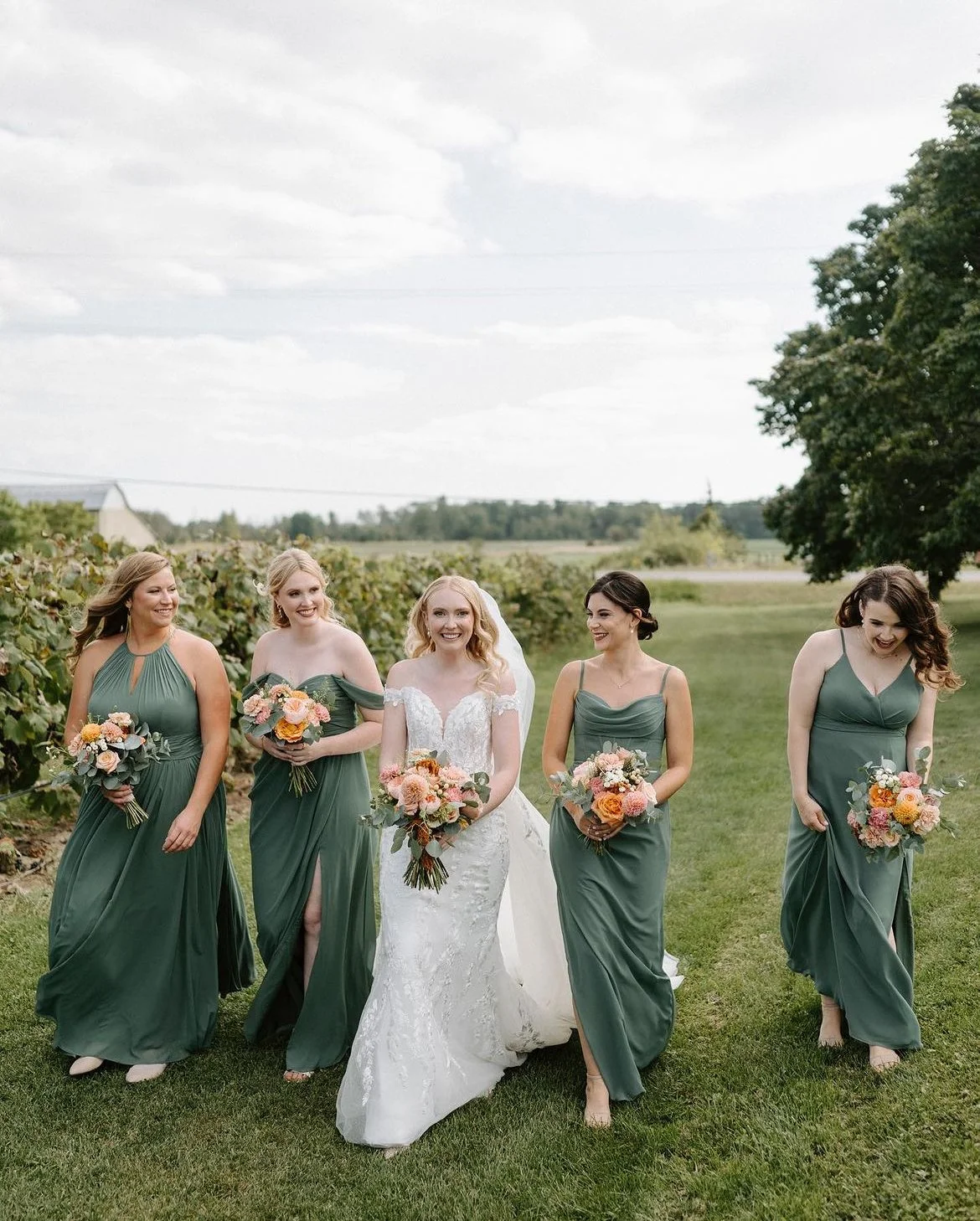 Bride and bridesmaids in green dresses walking outdoors, holding bouquets.