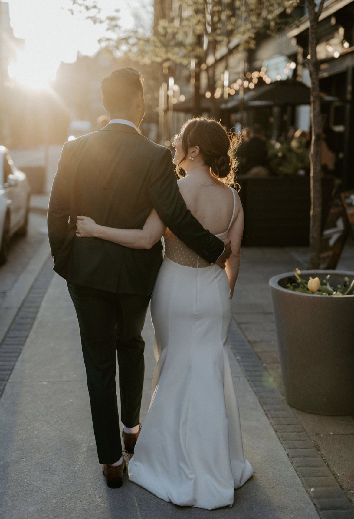 Couple in formal attire walking down a street at sunset.