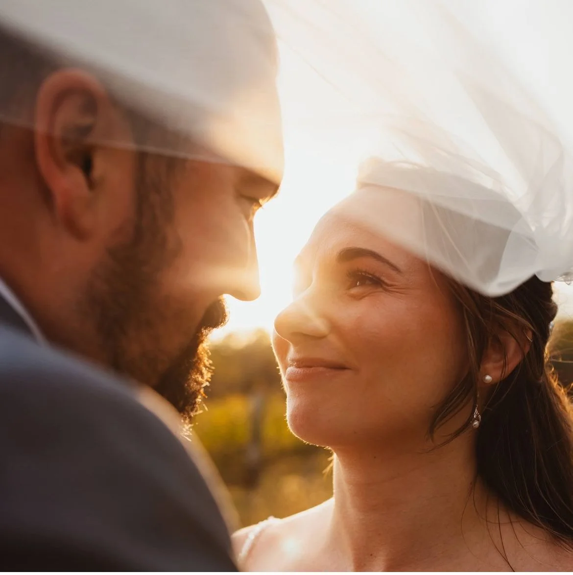 Bride and groom looking at each other with sunlight in the background, bride wearing a veil.