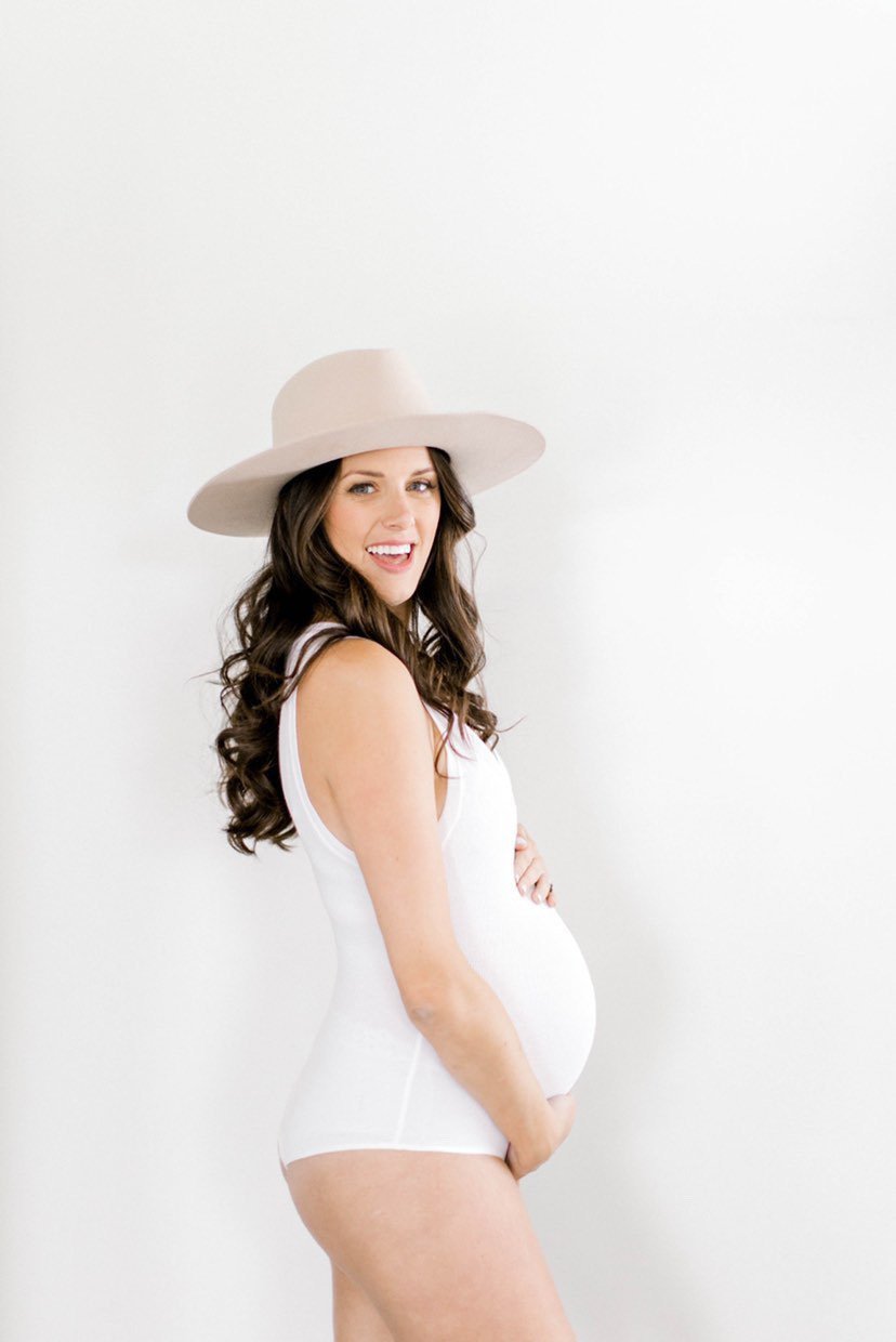 Pregnant woman in white outfit and hat smiling