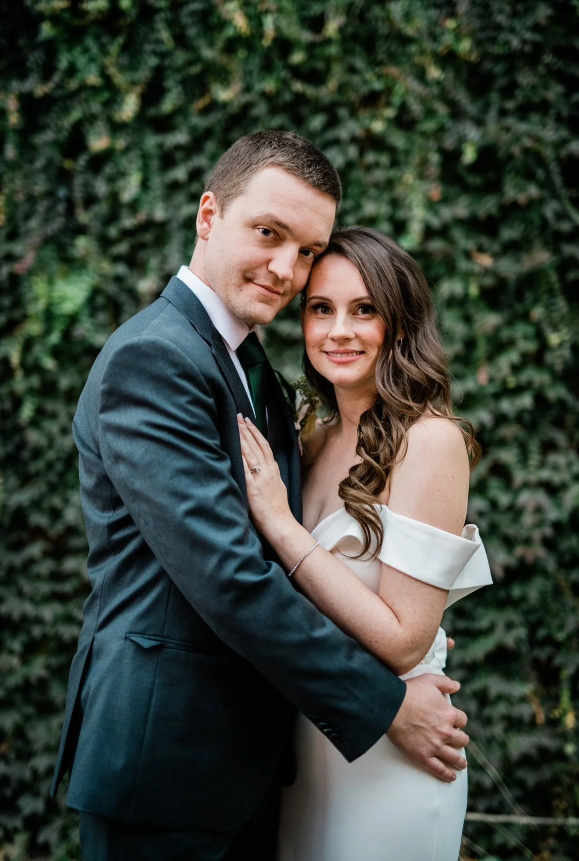 Bride and groom embracing in front of a leafy background.