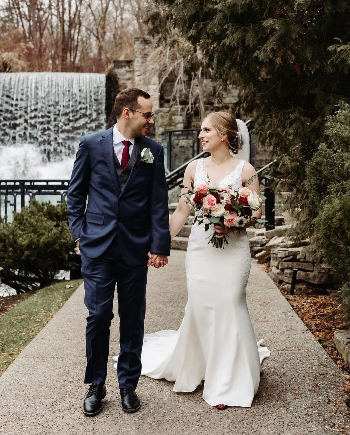 Bride and groom holding hands in a park setting with waterfall in background.