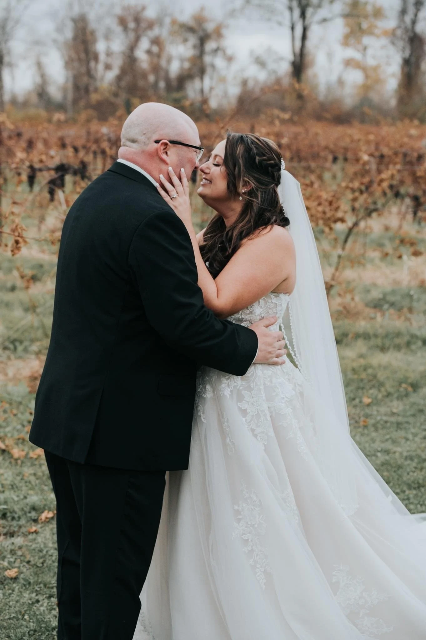 Bride and groom embracing outdoors with autumn foliage in the background.