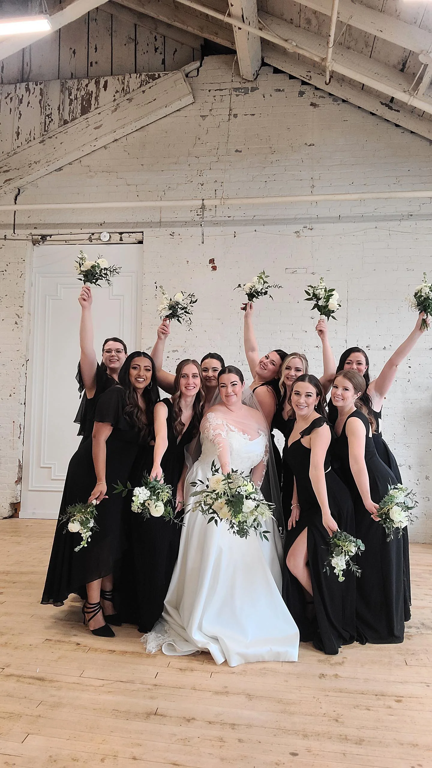 Bride and bridesmaids posing indoors, wearing black dresses, holding bouquets.