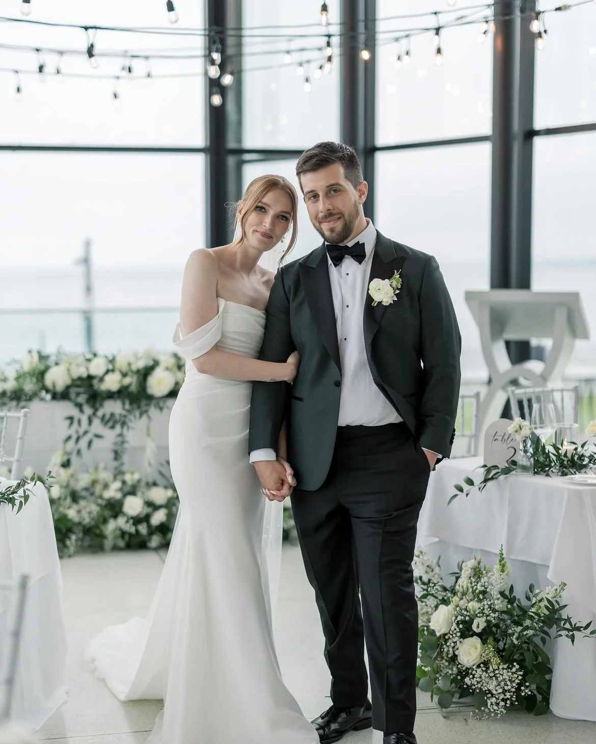 Bride and groom in a wedding venue with floral decorations and string lights.