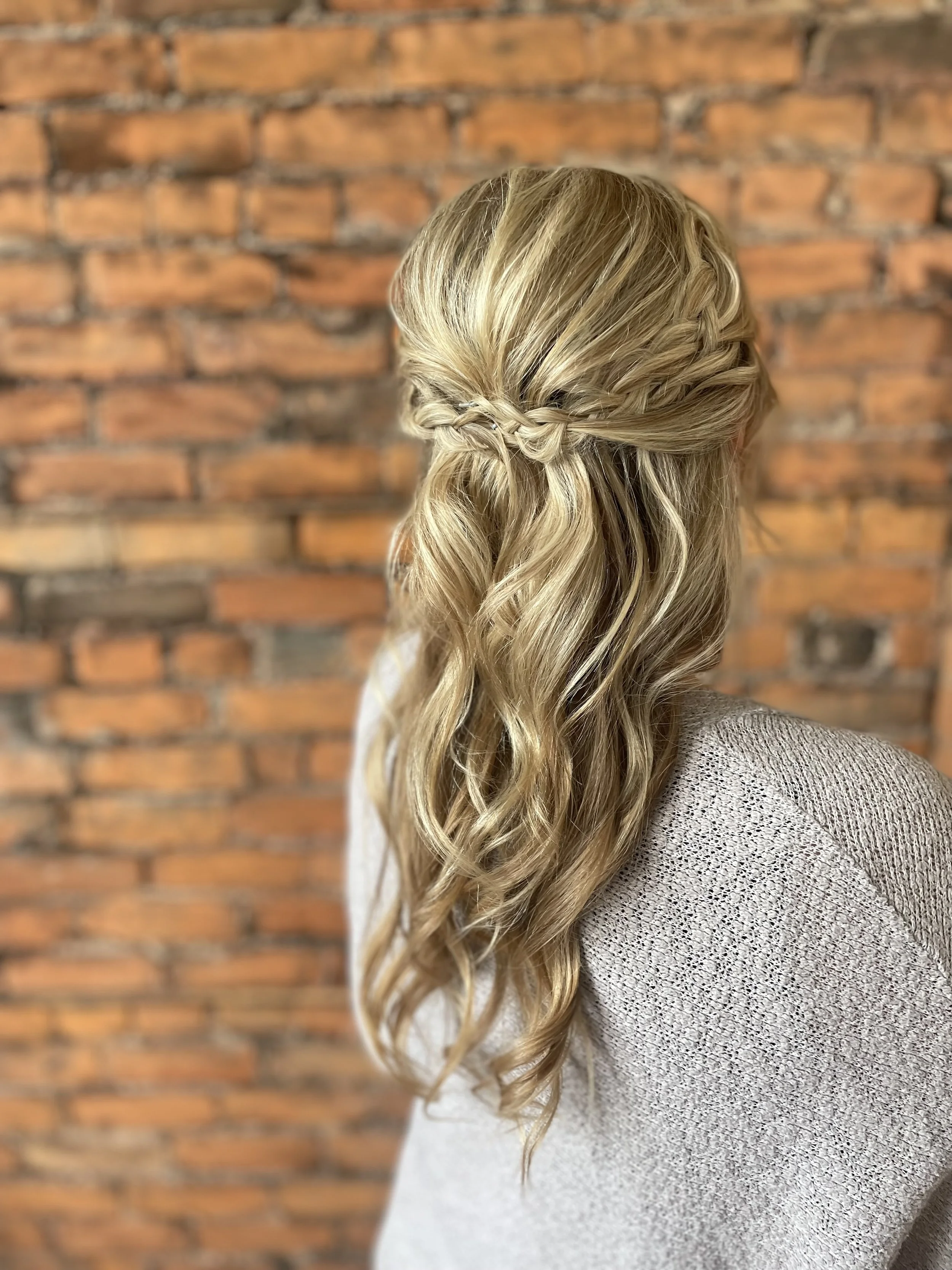 Blonde woman with braided half-up hairstyle against brick wall