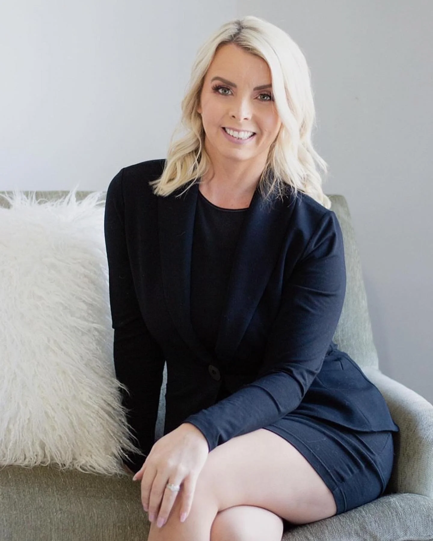 Smiling woman in black blazer sitting on a couch.