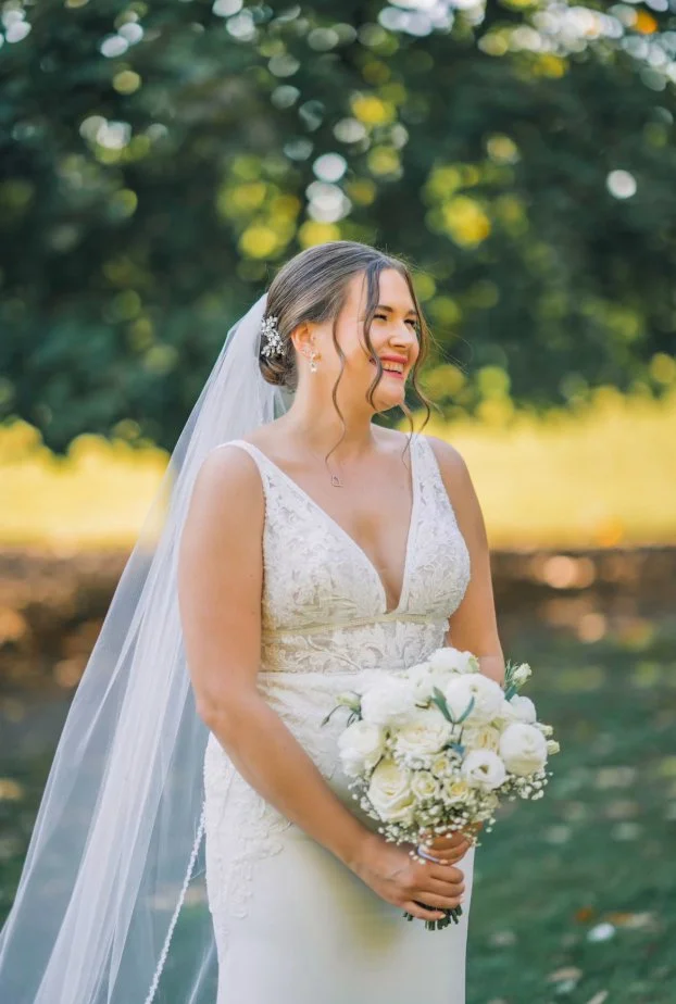 Bride in white wedding dress holding a bouquet of white flowers outdoors