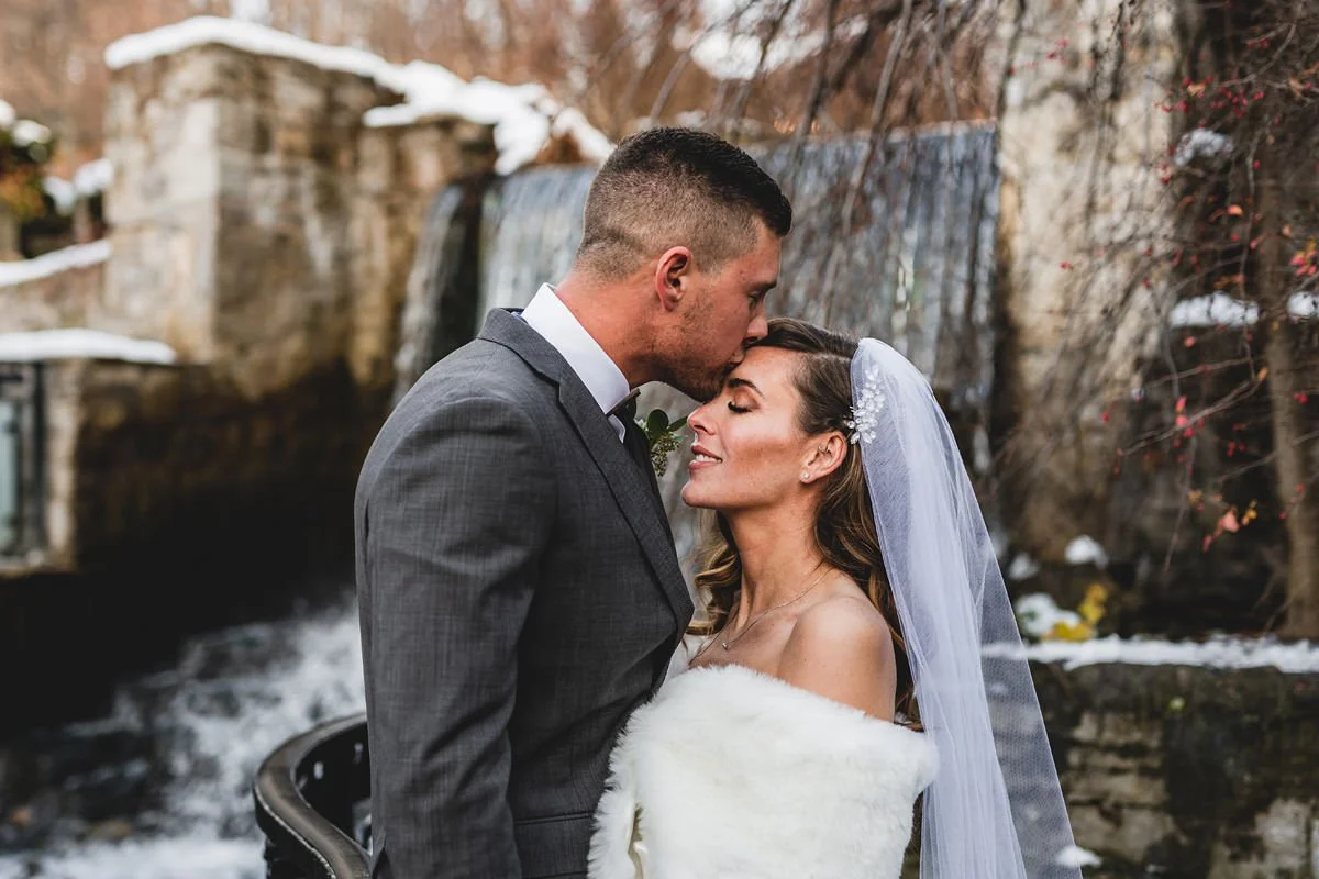 Bride and groom embracing by a snowy waterfall.