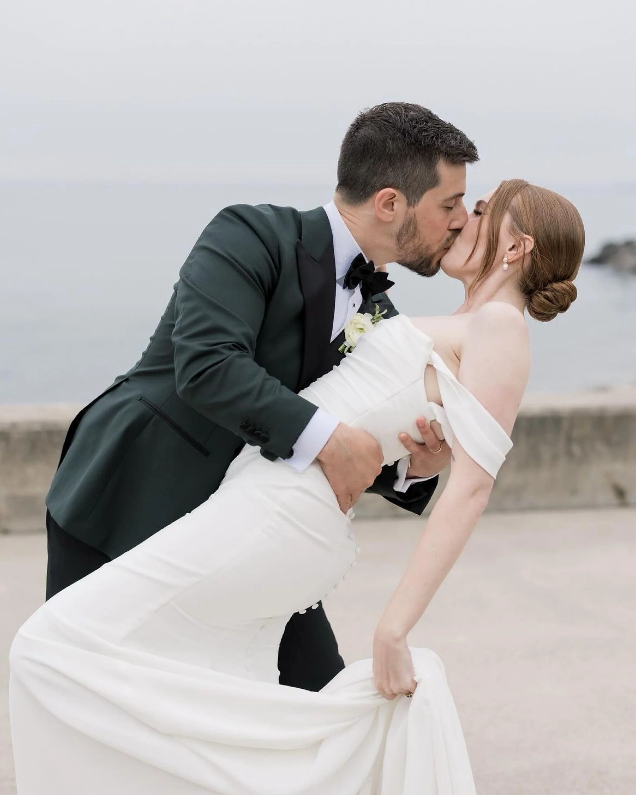 Bride and groom kissing, groom wearing black tuxedo, bride in white dress.