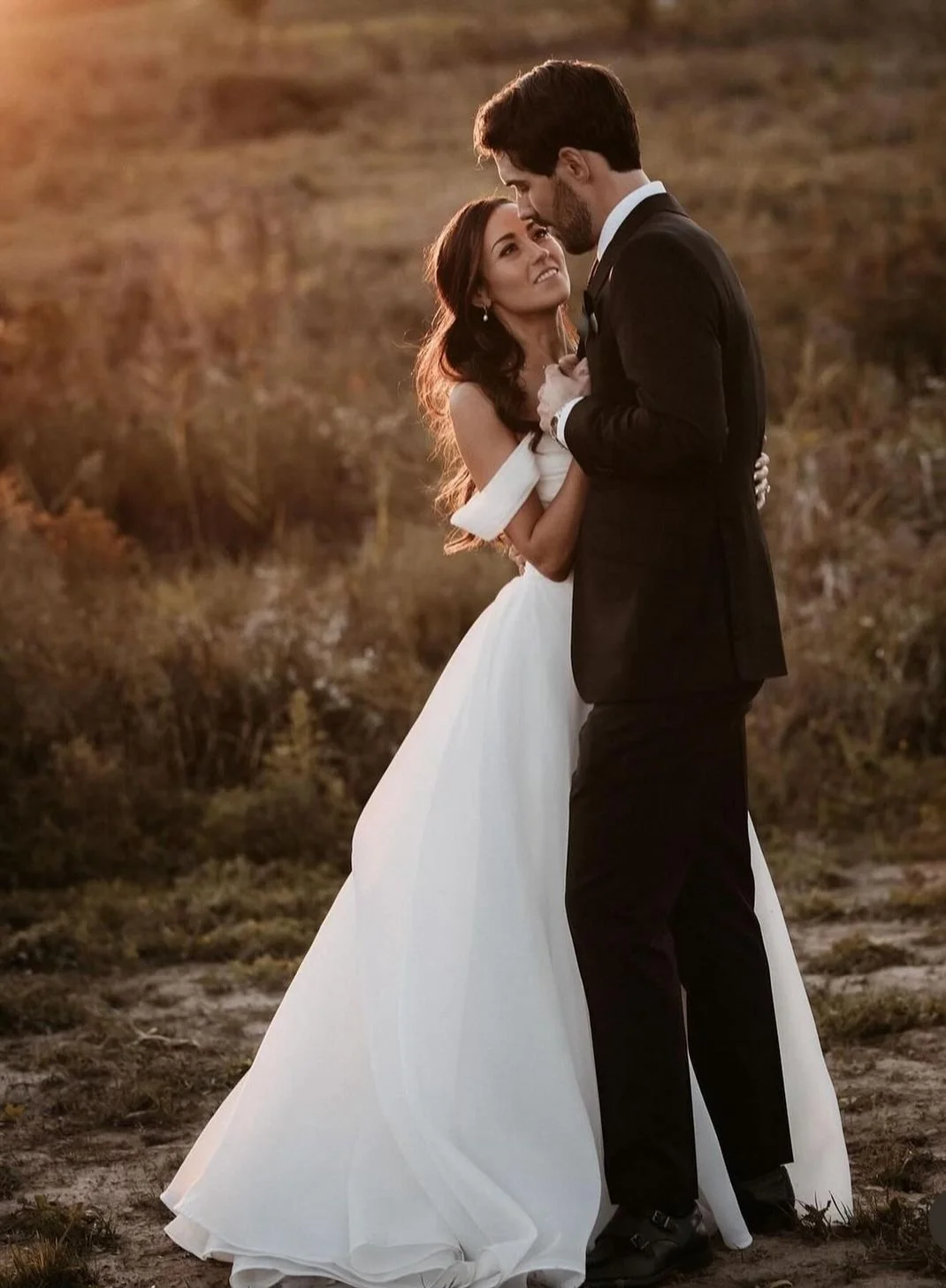 Bride and groom embracing outdoors at sunset in a romantic setting.