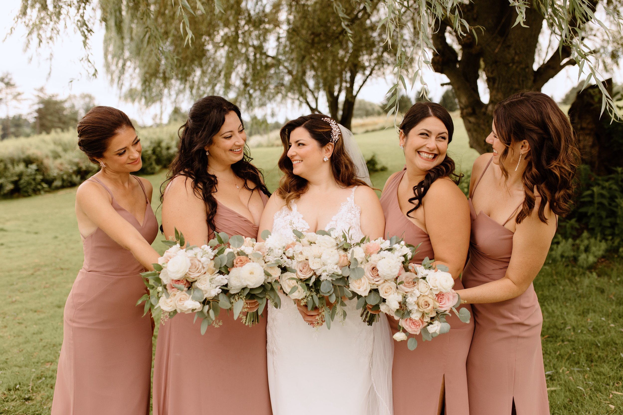 Bride with bridesmaids in pink dresses holding bouquets outdoors.