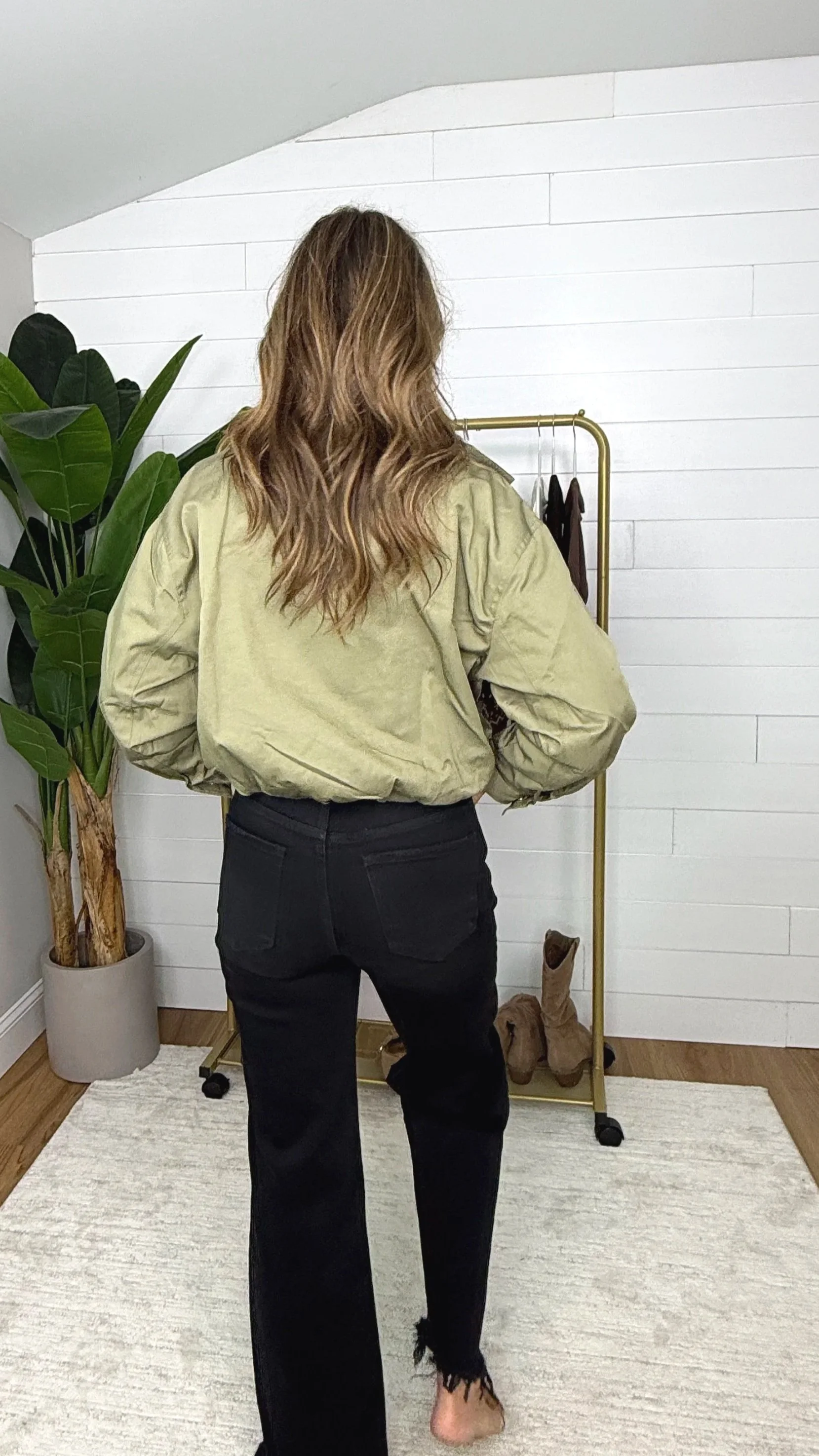 Back view of olive cropped zip up jacket showing elastic hem styled with black wide leg pants