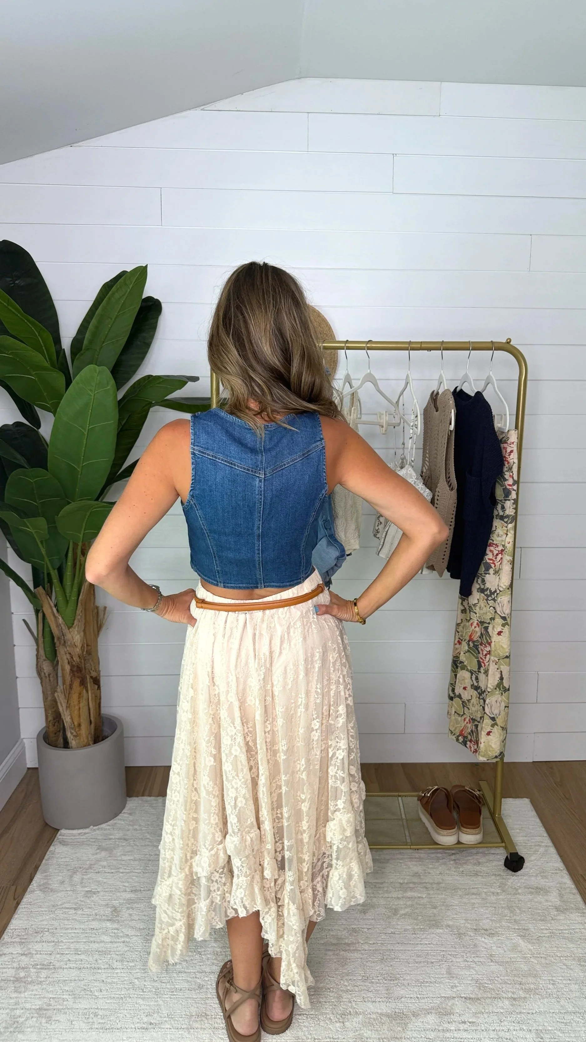 Back view of cream allover lace sharkbite midi skirt styled with denim crop vest and tan belt