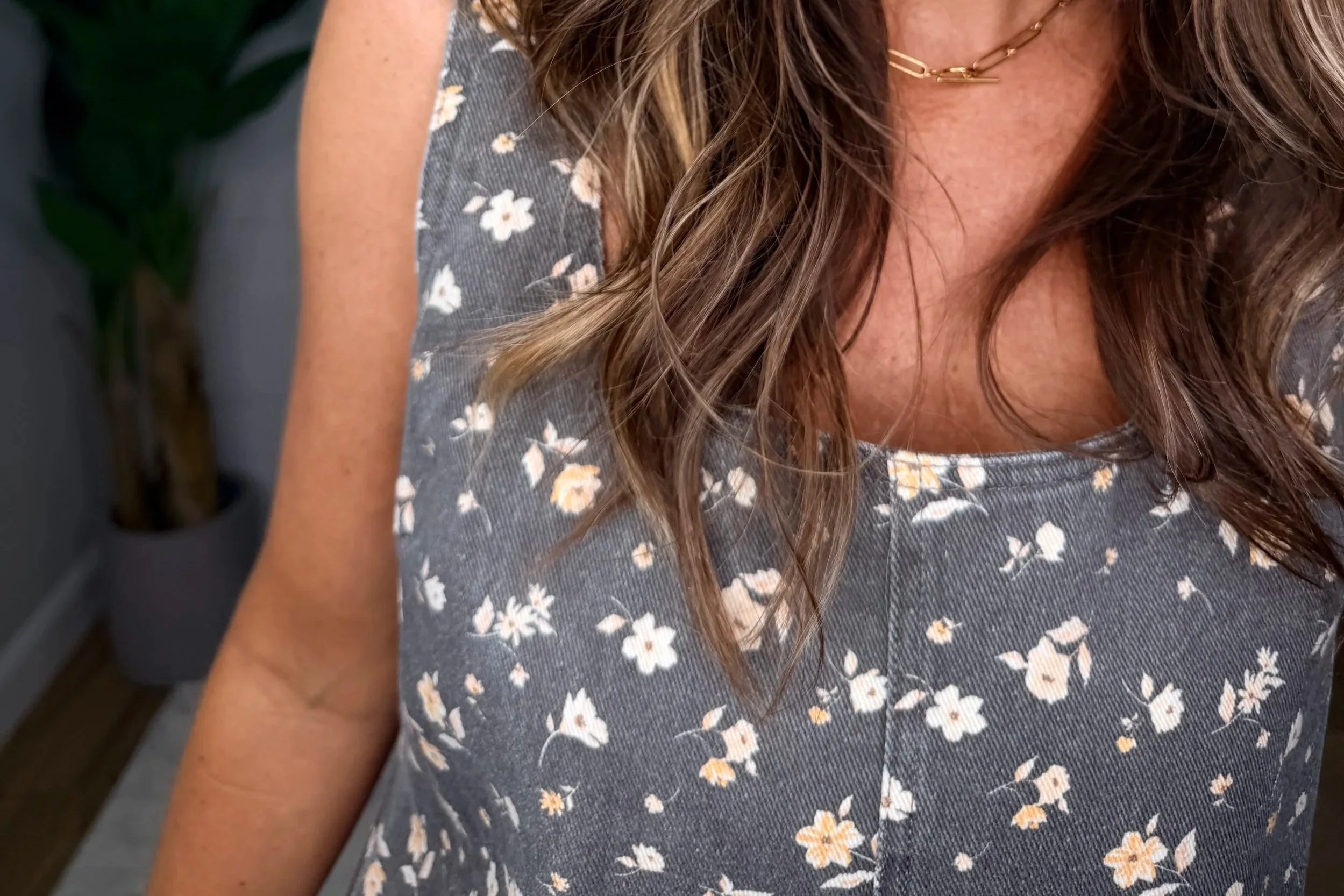 Close-up of a smiling model in a brown floral denim dress with a square neckline, gold hoop earrings and a gold paperclip necklace