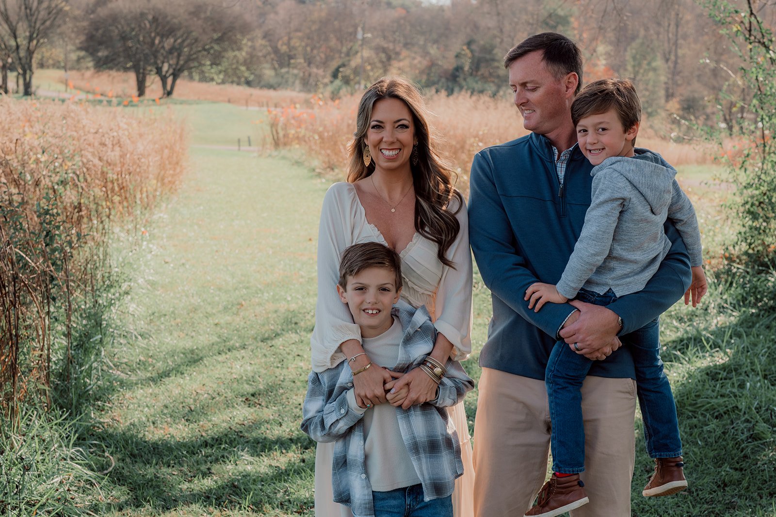 Family of four enjoying an outdoor walk in a park with autumn foliage, smiling and posing for the camera.