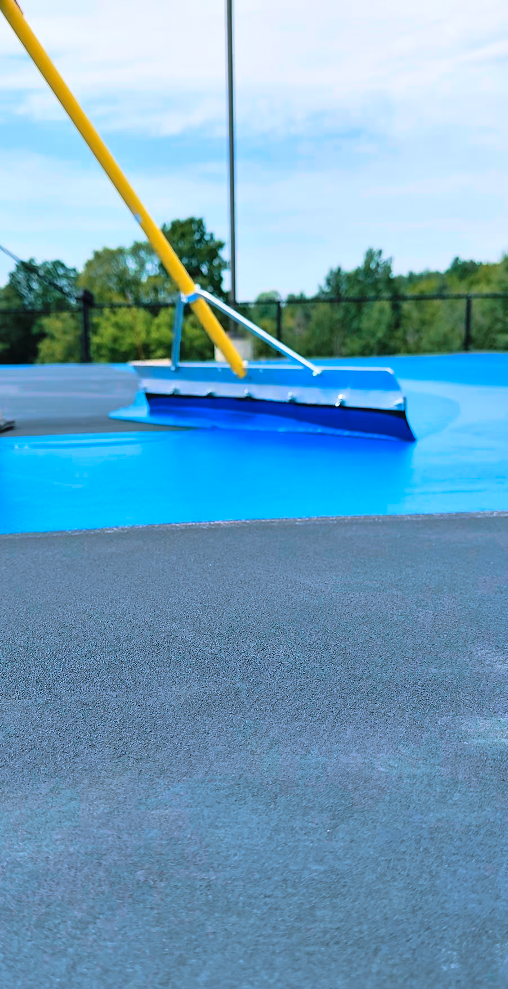 Close-up of a blue cleaning tool smoothing a blue surface, with a background of trees and a fence.